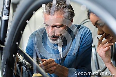 Senior mechanic working on bicycle woman watching Stock Photo