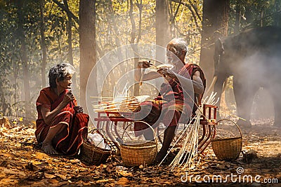 Senior Men and women are weaves basket with a large elephant in the background. Old man and woman weaves bamboo basket or fish Stock Photo