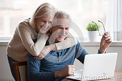 Senior middle aged happy couple embracing using laptop together Stock Photo