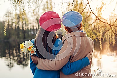 Senior mother with flowers and her adult daughter hugging by spring river. Mother`s day concept. Family values Stock Photo