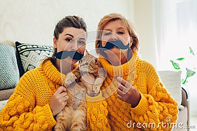 Senior mother and her adult daughter taking selfie with cat using photo booth props at home. Mother`s day concept Stock Photo