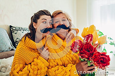 Senior mother and her adult daughter taking selfie with flowers using photo booth props at home. Mother`s day concept Stock Photo