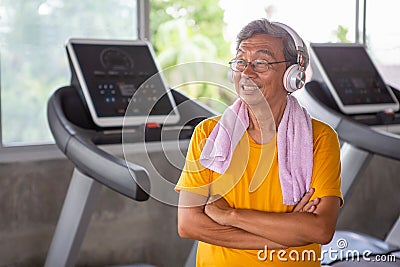Senior older man taking a break from workout listening music with headphones relaxing in fitness gym. aged . Old male .Mature Stock Photo