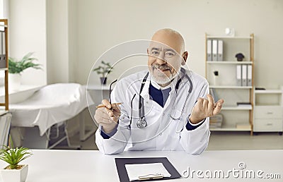Senior online doctor sitting at desk and giving telemedicine consultation via video call Stock Photo