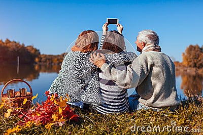 Senior parents taking selfie by autumn lake with their adult daughter. Family values. People having picnic Stock Photo