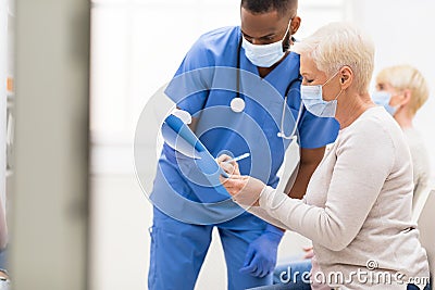 Senior Patient Signing Papers With Doctor Before Coronavirus Vaccination Indoor Stock Photo