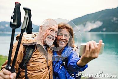 A senior pensioner couple standing by lake in nature, taking selfie. Stock Photo