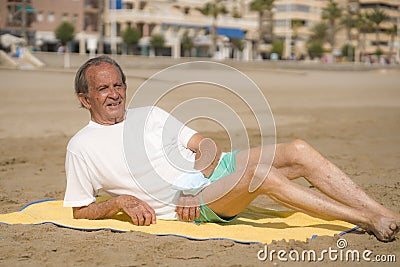 Senior pensioner sitting relaxed on the beach - retired old man on his 70s looking at the sea thoughtful and contemplative with Stock Photo