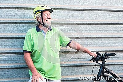 Senior people grandfather standing close to his e bike. Healthy lifestyle for retired person. Yellow helmet. Metal wall in Stock Photo