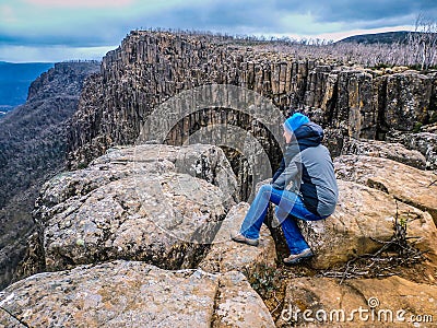 Senior perched on rocks at Devil`s Gullet, Tasmania, looking out into a steep, glacial gorge formed by vertical dolerite cliffs Stock Photo