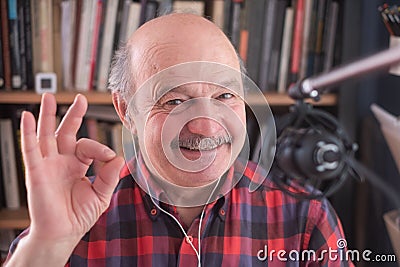 Senior retired man blogger looking at camera recording vlog, smiling old elder grandfather showing ok gesture Stock Photo