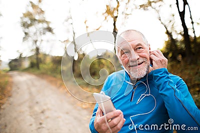 Senior runner in nature with smart phone with earphones. Stock Photo