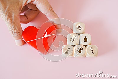 senior`s hand holding red heart with heartbeat and pyramid of health and medical icon on wood cubes on pastel pink background Stock Photo