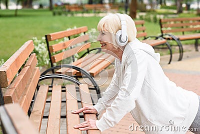 senior sportive woman in headphones training near benches Stock Photo