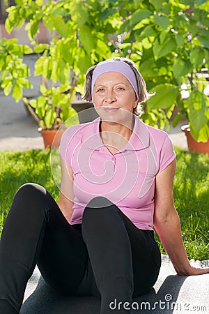 Senior sportive woman sitting on mat sunny Stock Photo