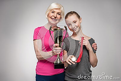 Senior sportswoman and girl holding trophy and medal on grey Stock Photo