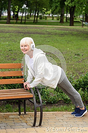 senior sportswoman in headphones doing push up near bench Stock Photo