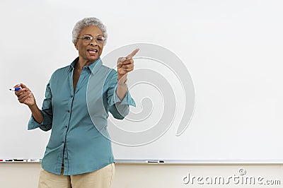 Senior teacher pointing while gesturing against white board in classroom Stock Photo