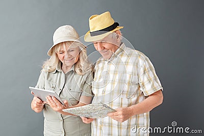 Senior tourists in beach hats studio standing on gray holding map and browsing internet on digital tablet Stock Photo