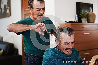 Senior twin cutting his brother`s hair at home during coronavirus lockdown - Focus on right man Stock Photo