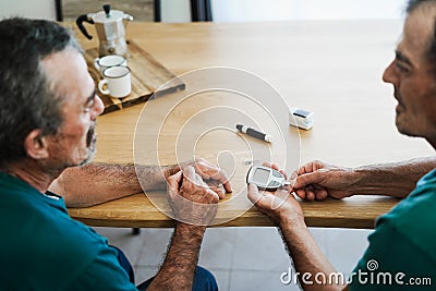 Senior twin men making blood glycemia test for diabetes check - Focus on hand holding glucometer Stock Photo