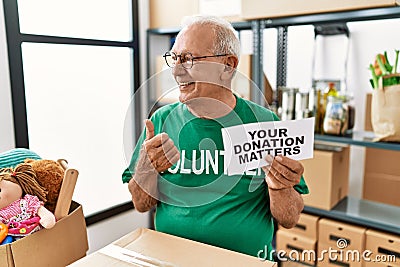 Senior volunteer man holding your donation matters pointing thumb up to the side smiling happy with open mouth Stock Photo