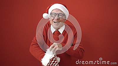 senior wearing christmas hat looking inside of sock over isolated red background Stock Photo