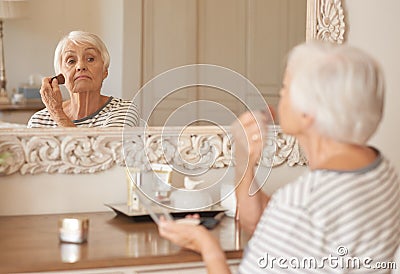 Senior woman applying makeup to her cheek in a mirror Stock Photo