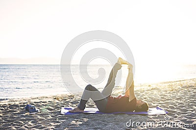 Senior woman exercising, stretching on yoga mat at the beach, doing leg raises Stock Photo