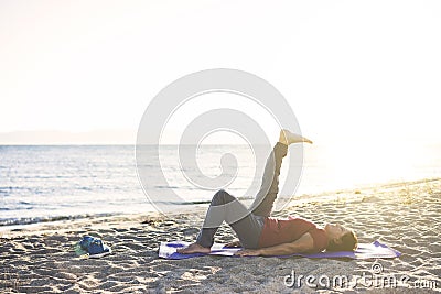 Senior woman exercising, stretching on yoga mat at the beach, doing leg raises Stock Photo