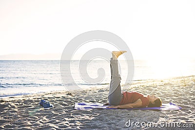 Senior woman exercising, stretching on yoga mat at the beach, doing leg raises Stock Photo