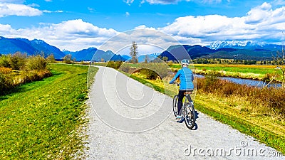 Senior woman biking along the Alouette River on the dyke surrounding Pitt Polder at the town of Maple Ridge in British Columbia Editorial Stock Photo