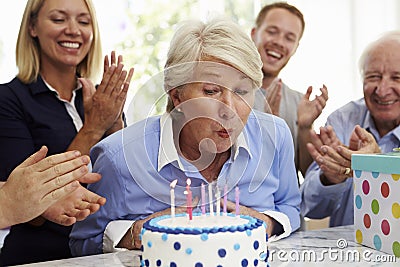 Senior Woman Blows Out Birthday Cake Candles At Family Party Stock Photo