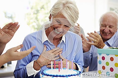 Senior Woman Blows Out Birthday Cake Candles At Family Party Stock Photo