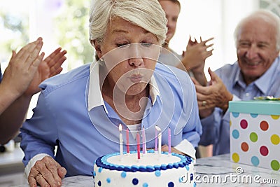 Senior Woman Blows Out Birthday Cake Candles At Family Party Stock Photo