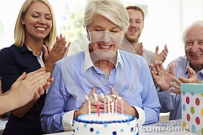 Senior Woman Blows Out Birthday Cake Candles At Family Party Stock Photo