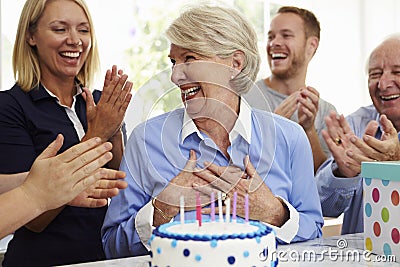 Senior Woman Blows Out Birthday Cake Candles At Family Party Stock Photo