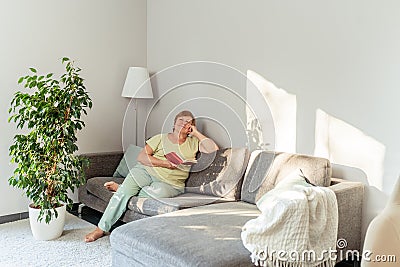 Senior woman daydreaming while relaxing and reading at home Stock Photo