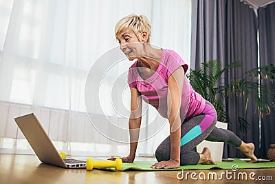 Senior woman doing stretching exercises in front of laptop at home, watching online tutorials Stock Photo