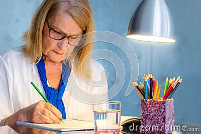 Senior woman drawing in color book for adults. Stock Photo