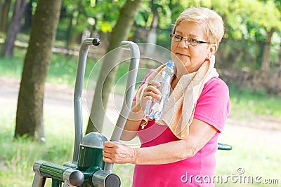 Senior woman drinking water after exercise on outdoor gym, healthy lifestyle Stock Photo
