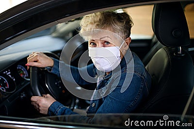 Senior woman driver with face mask in car, quarantine concept. Stock Photo