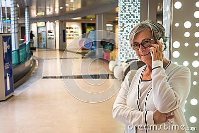 A senior woman with gray hair and eyeglasses standing in a shopping mall. Talking at cellphone Stock Photo