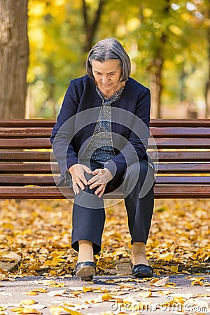 Senior woman having knee pain sitting on bench in park Stock Photo