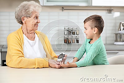 Senior woman with her grandson using digital glucometer at home Stock Photo