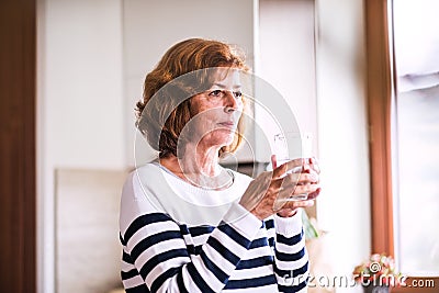 Senior woman holding a glass of water in the kitchen. Stock Photo