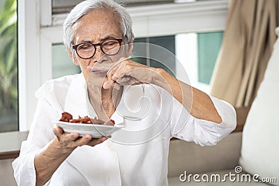 Senior woman holding plate of bad spoiled or expired food in her hand,rotten food,emitting a fetid smell or strong-smelling food, Stock Photo