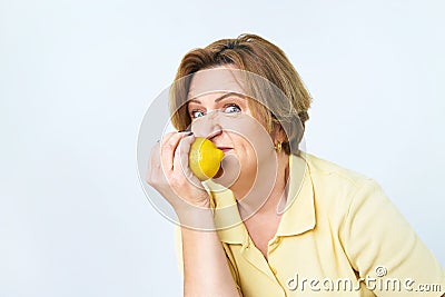 Senior woman with lemon in hand doing funky action. An elderly woman is eating a lemon. She is on a diet. She is looking Stock Photo