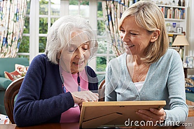 Senior Woman Looks At Photo In Frame With Mature Female Neighbor Stock Photo