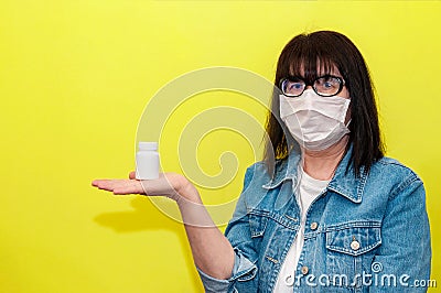 Senior Woman in Protective Face Mask Keeps Hand Pills Jar on Yellow Background Stock Photo